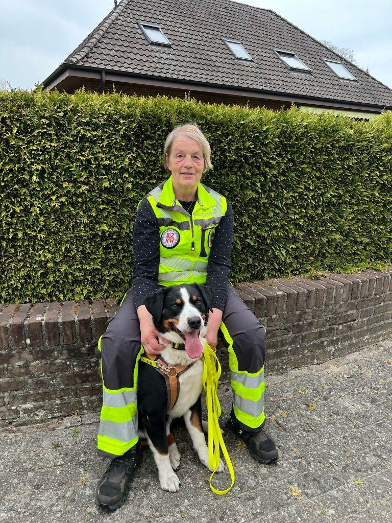 Mitglied der S.A.R. Suchhundestaffel Nordwest sitzt auf einer niedrigen Mauer mit ihrem Suchhund, beide machen eine Pause nach dem Einsatz.